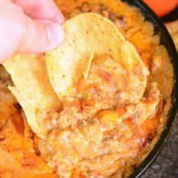 scooping some taco dip from the skillet with two round tortilla chips.