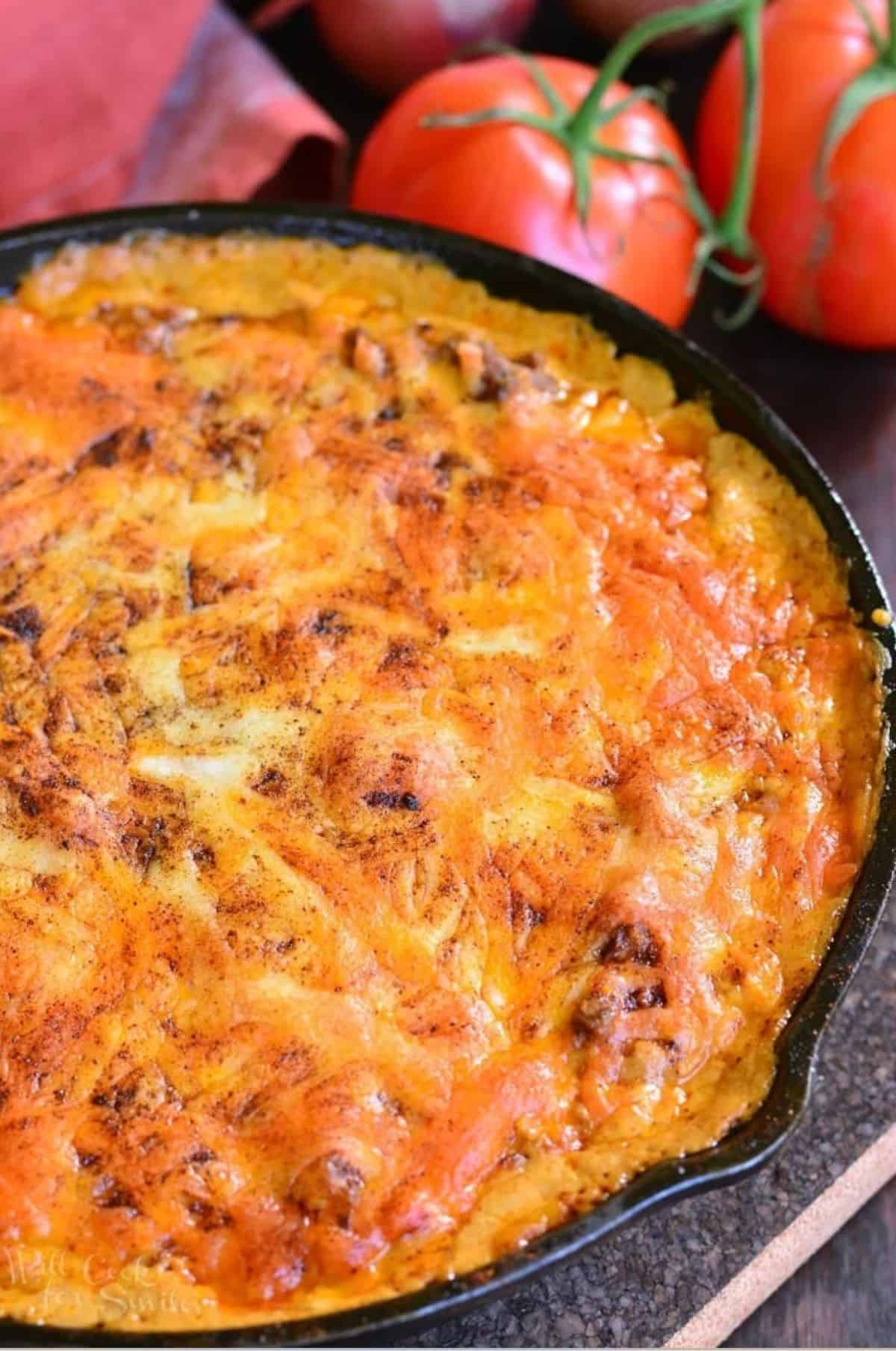 Beef taco dip baked in a skillet next to tomatoes on a vine.