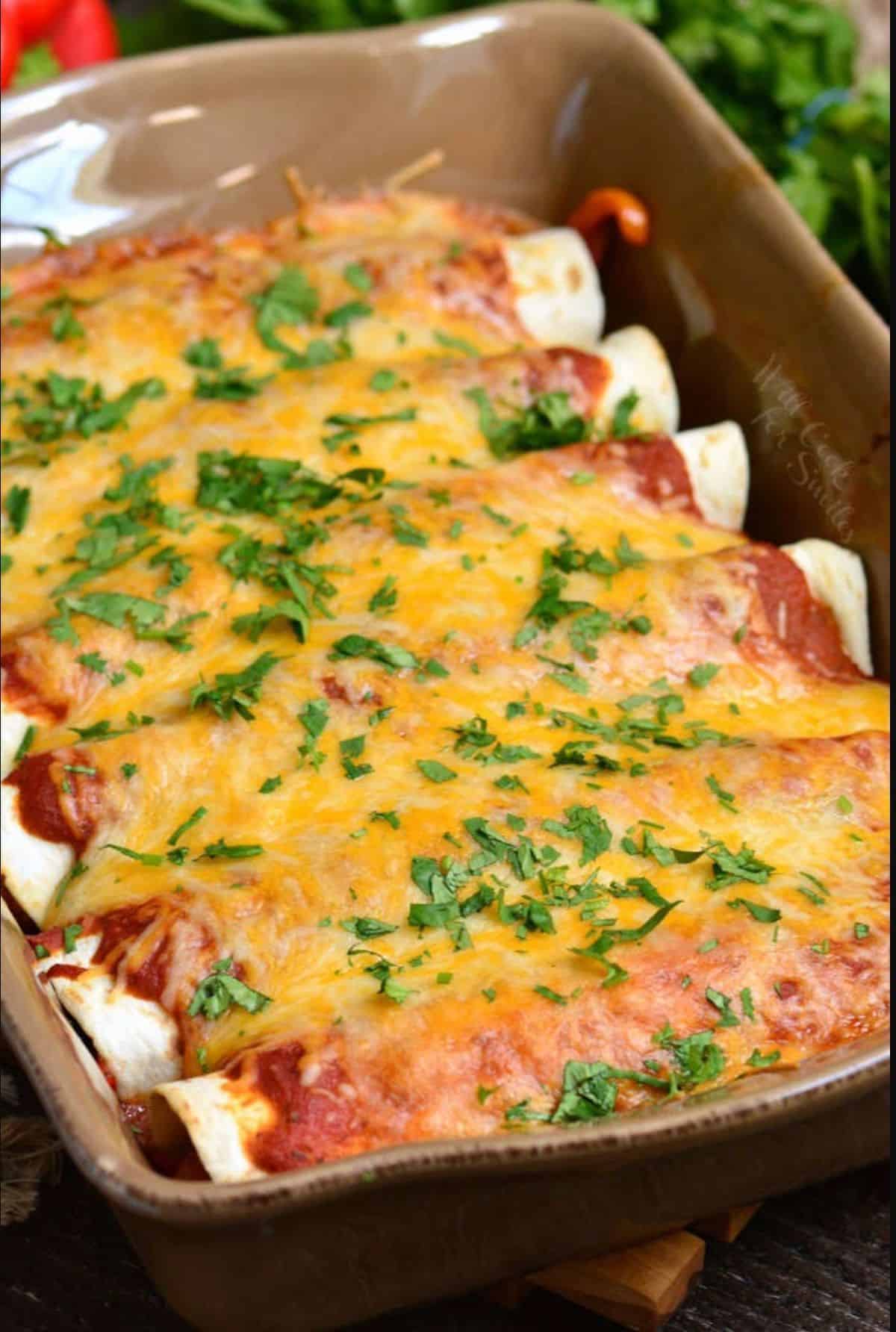 baked beef enchiladas topped with cilantro in a brown baking dish.