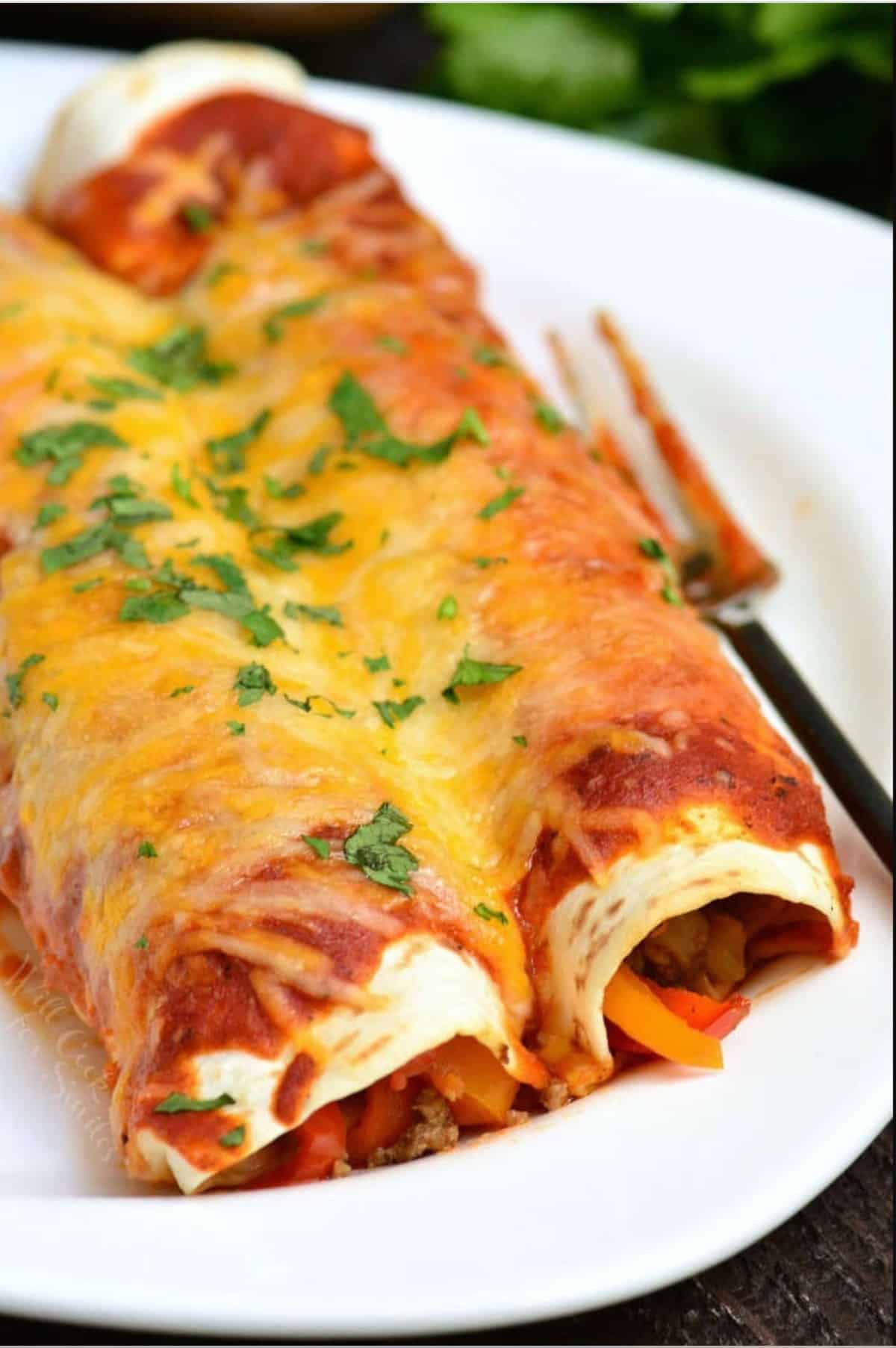 two cheesy beef enchiladas on a white plate with a fork.