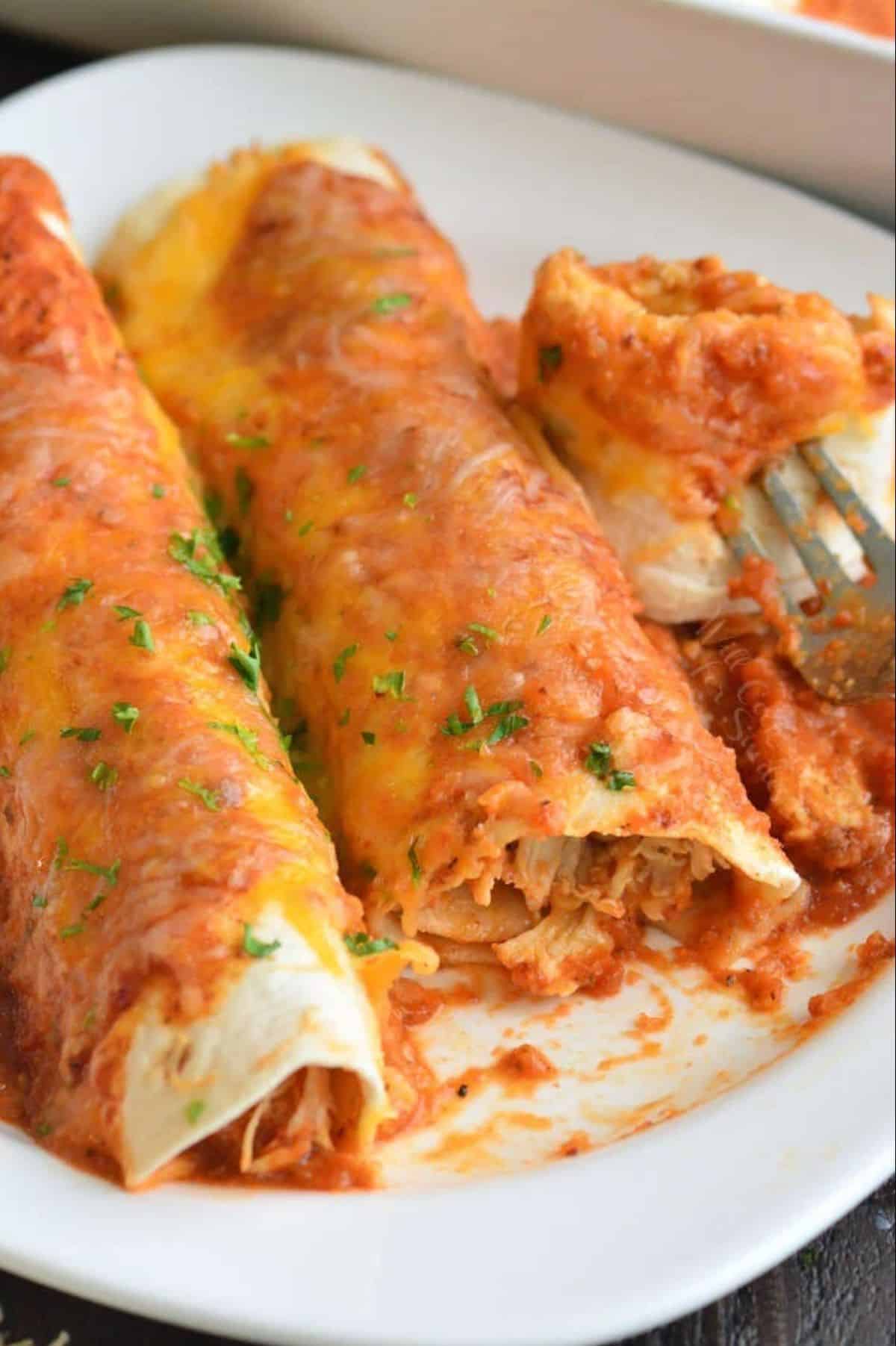 two enchiladas in a white plate with one bite taken out and visible.