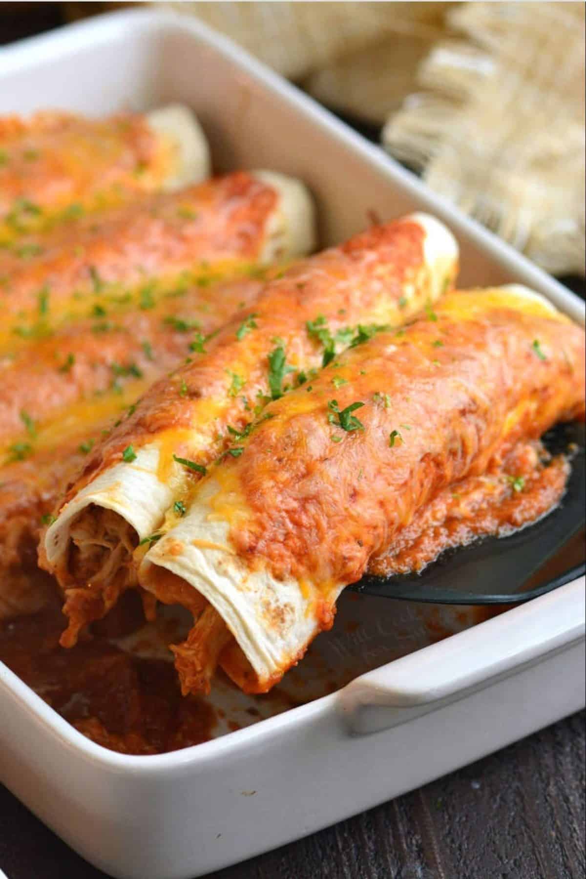 pulling out two chicken enchiladas from the baking dish with a spatula.