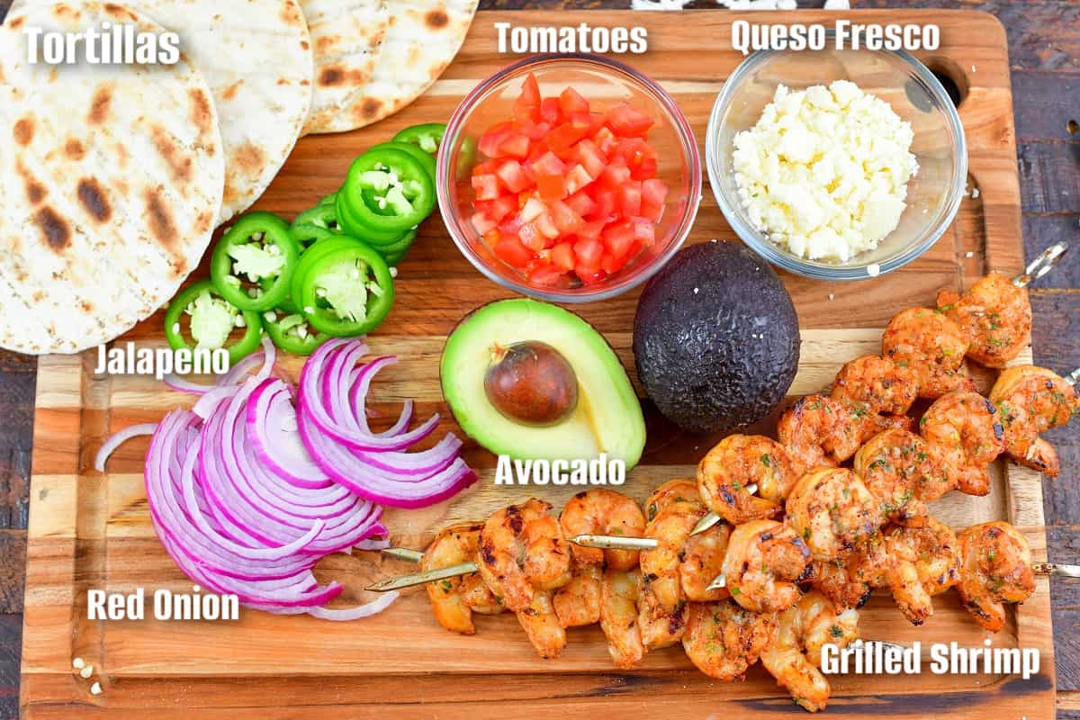 labeled ingredients for grilled shrimp tacos on a wooden cutting board.