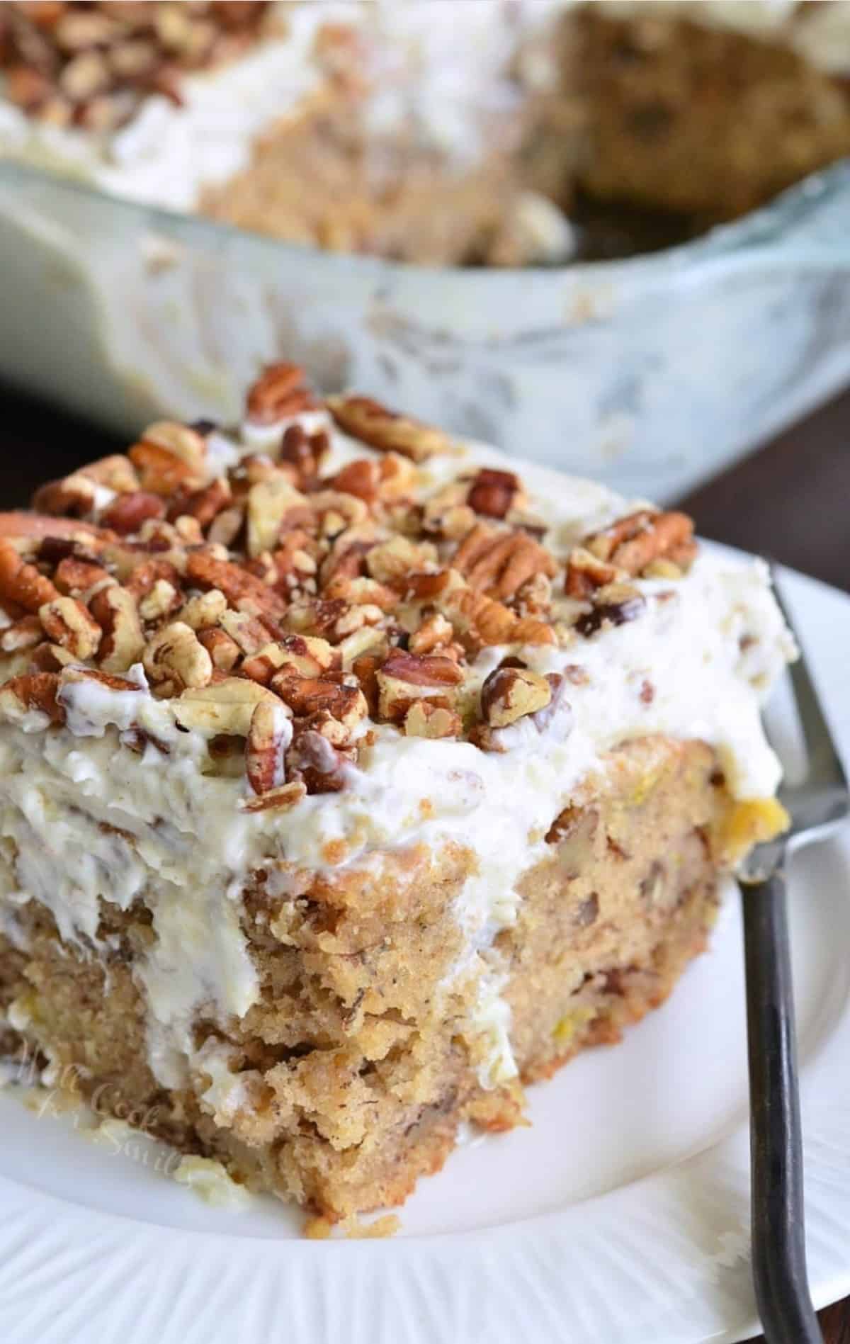 piece of poke cake on a white plate topped with nuts and a fork next to it.