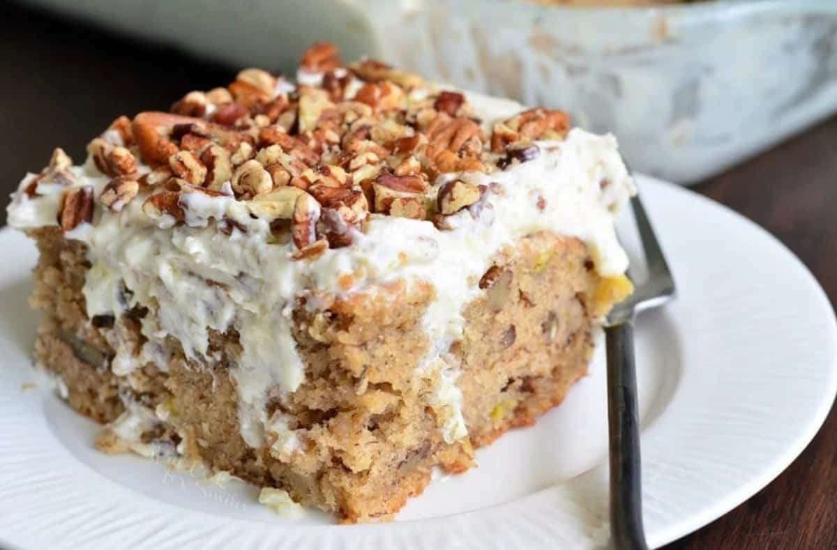 square piece of brown poke cake with whipped frosting and pecans on top.