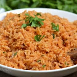 Red colored Spanish rice in a bowl with wooden spoon in the rice.