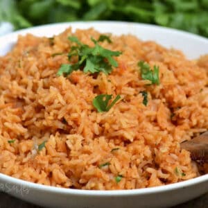 Red colored Spanish rice in a bowl with wooden spoon in the rice.