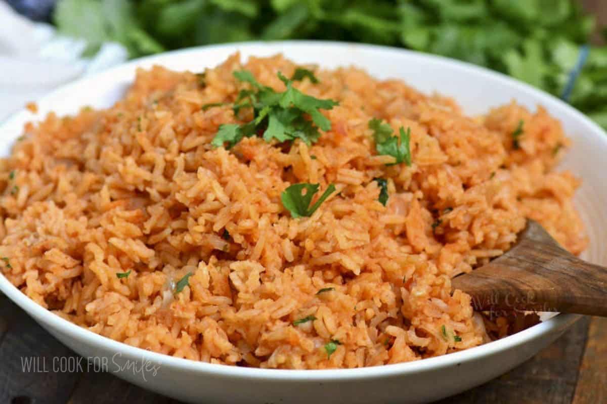 Red colored Spanish rice in a bowl with wooden spoon in the rice.