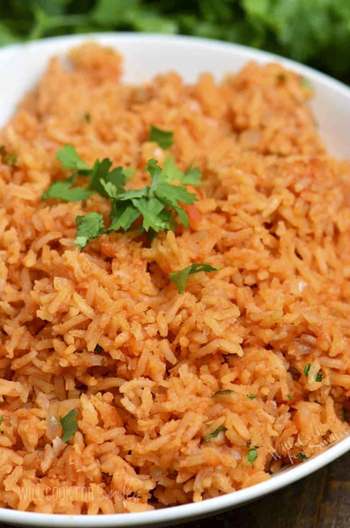 Redish colored Spanish rice in a bowl topped with cilantro.