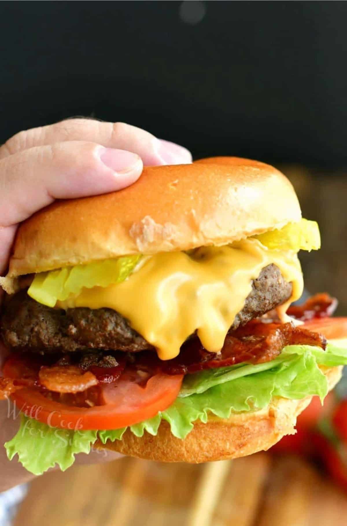 holding a cheeseburger with toppings with one hand.