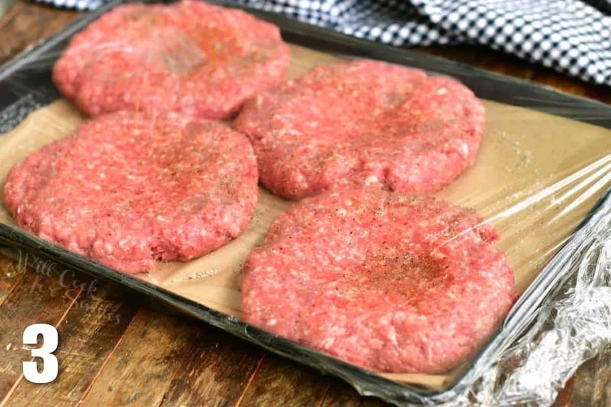 four raw burger patties under the plastic wrap with dent in the middle.