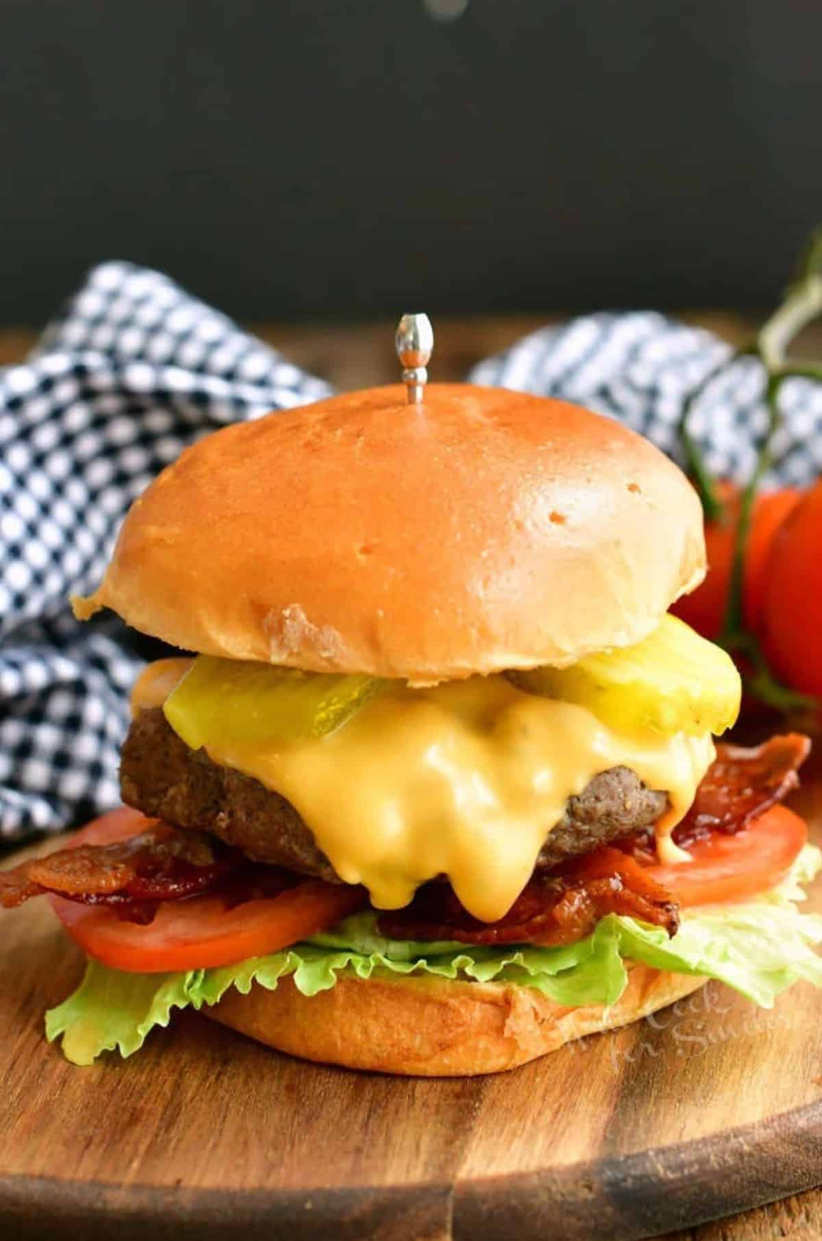 a cheeseburger with cheese, tomatoes, bacon, lettuce and pickles.