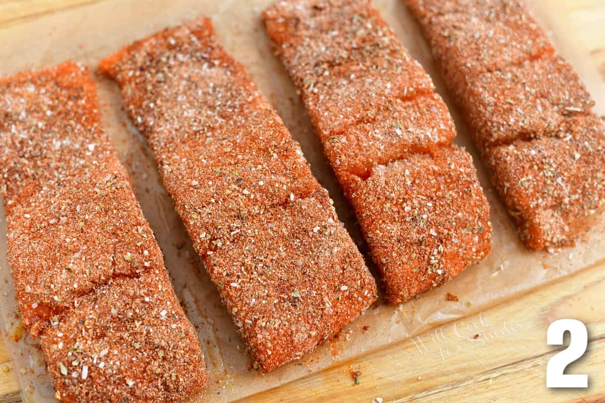 four seasoned salmon filets on parchment paper before baking.