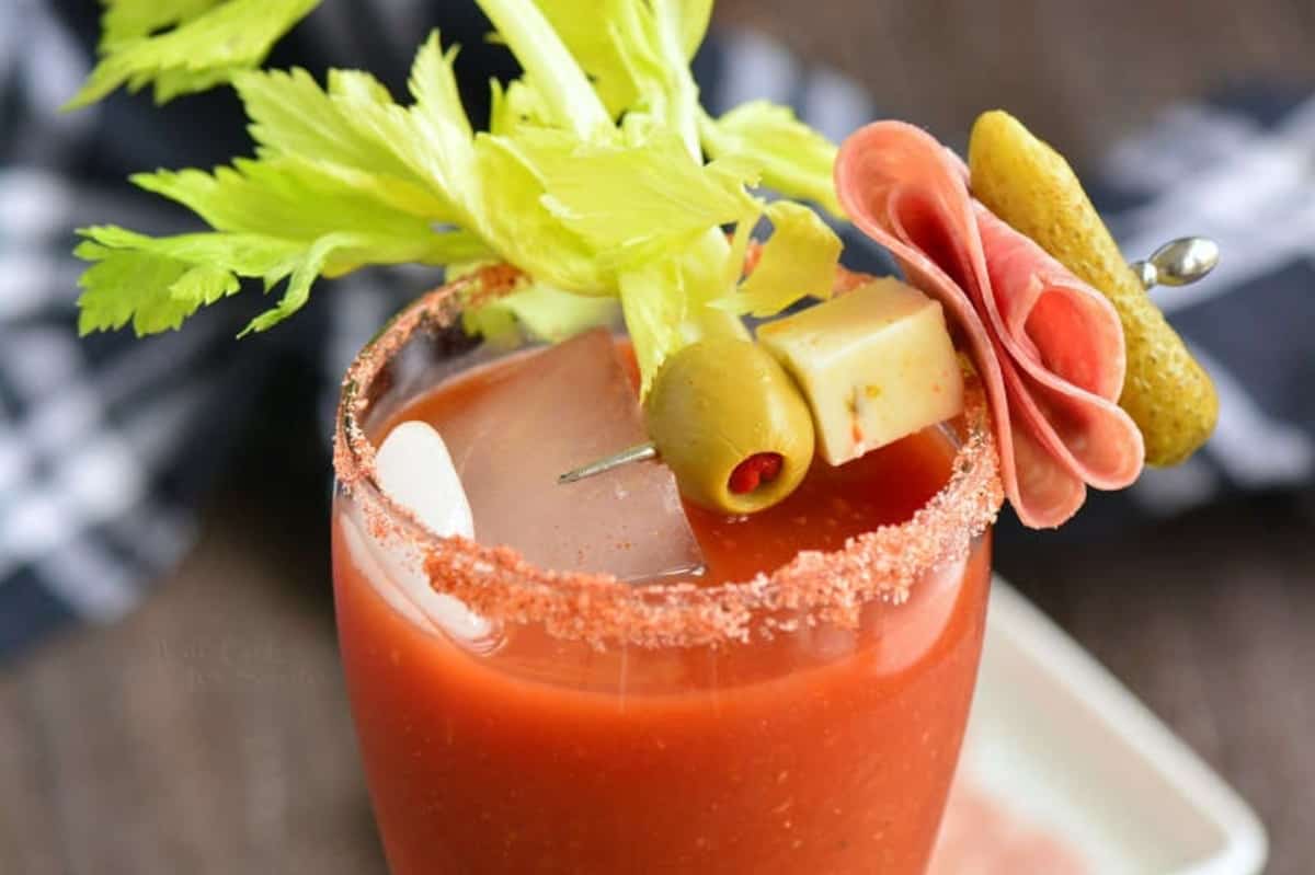 Garnish of cheese, olive, salami, and pickle over the top of a glass with Bloody Mary.