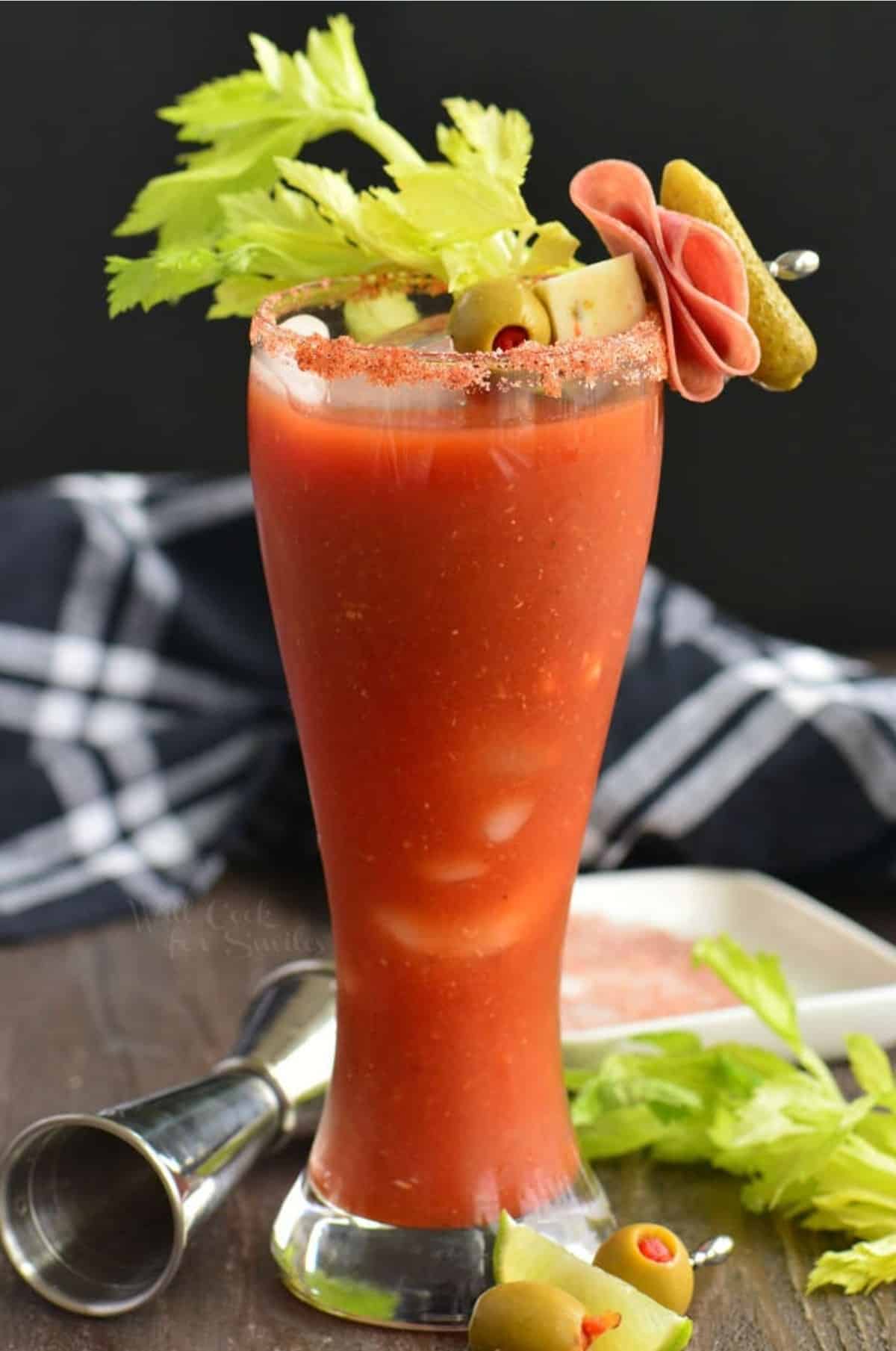 Tall glass of Bloody Mary with celery and a garnish of cheese, olive, salami, and pickle