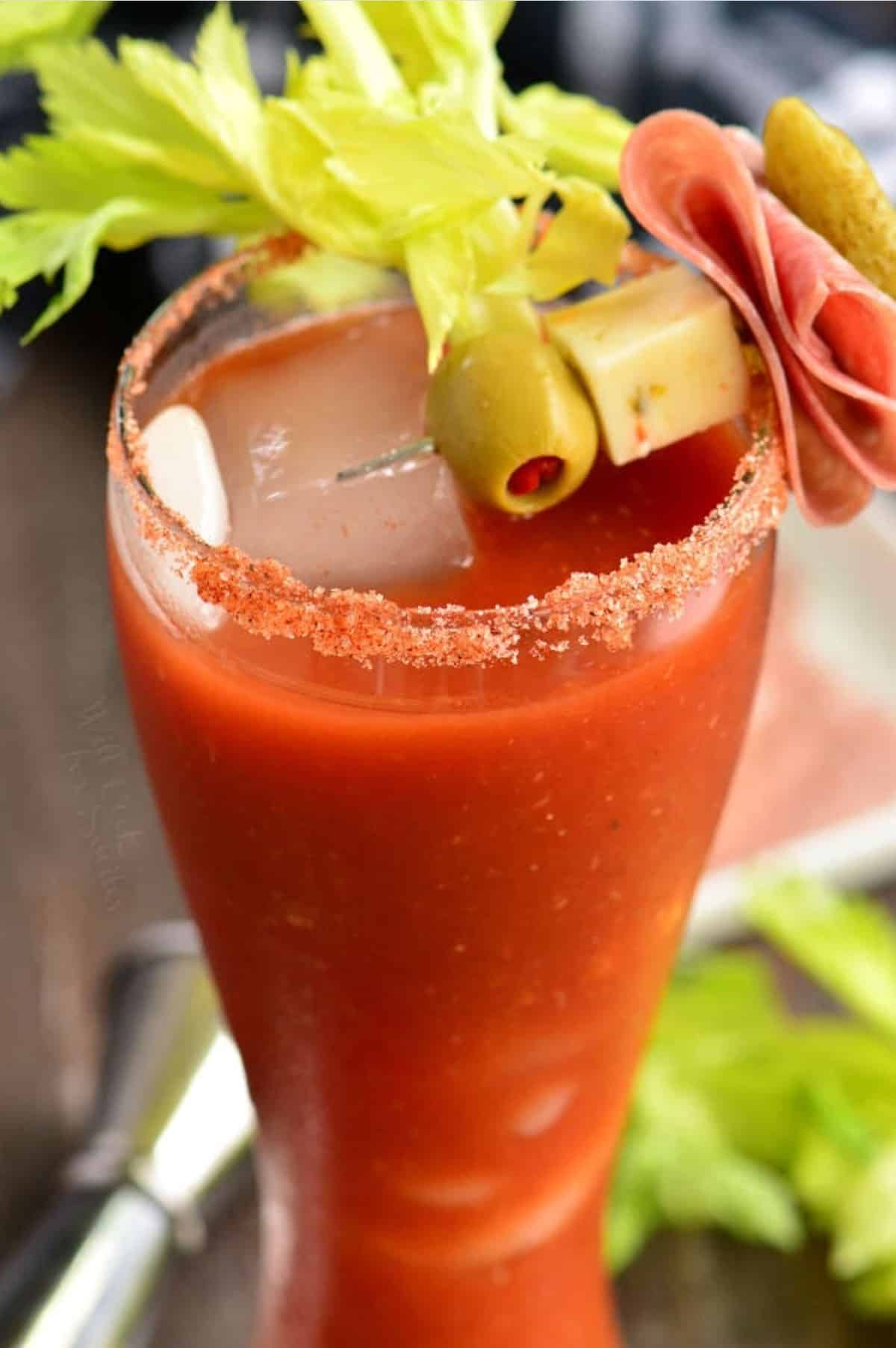 Bloody Mary cocktail with spicy salt rim and garnish of cheese, olive, salami, and pickle.