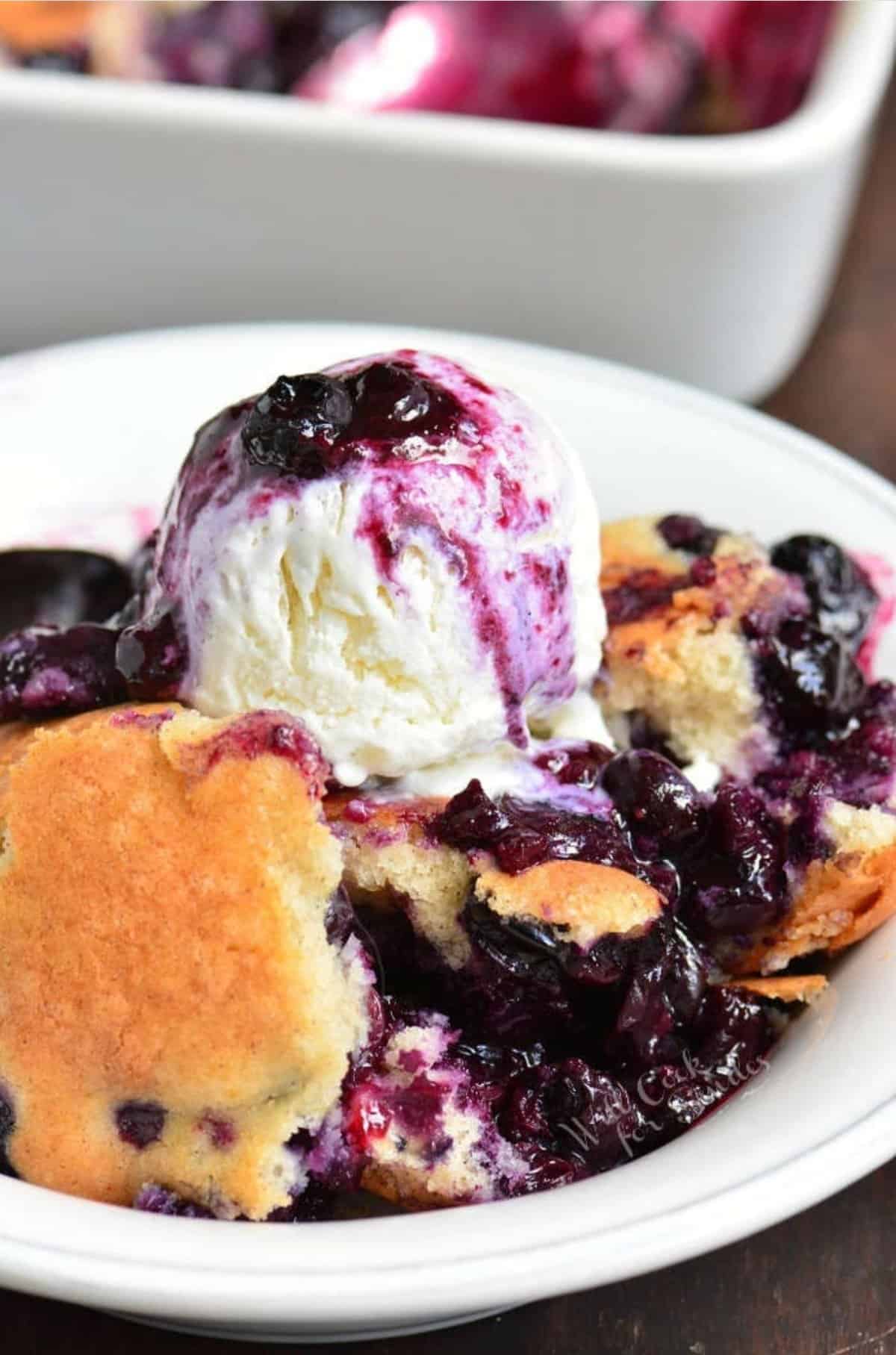 blueberry cobbled topped with ice cream in a white bowl.