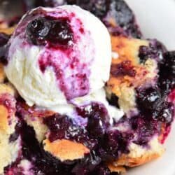 blueberry cobbler topped with ice cream in a white plate.