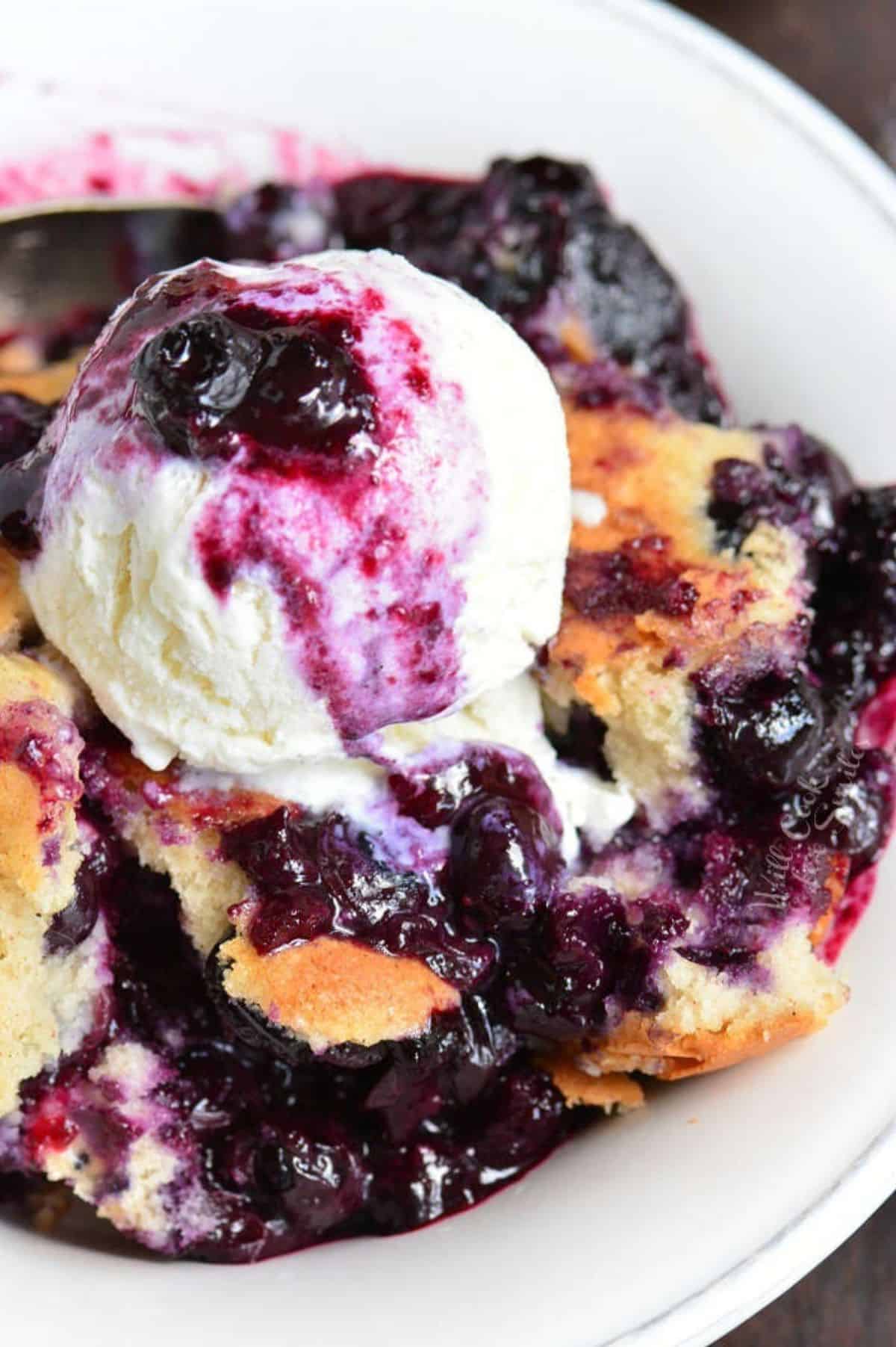 blueberry cobbler topped with ice cream in a white plate.