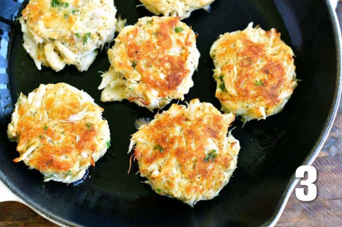 several crab cakes cooking in a black skillet.