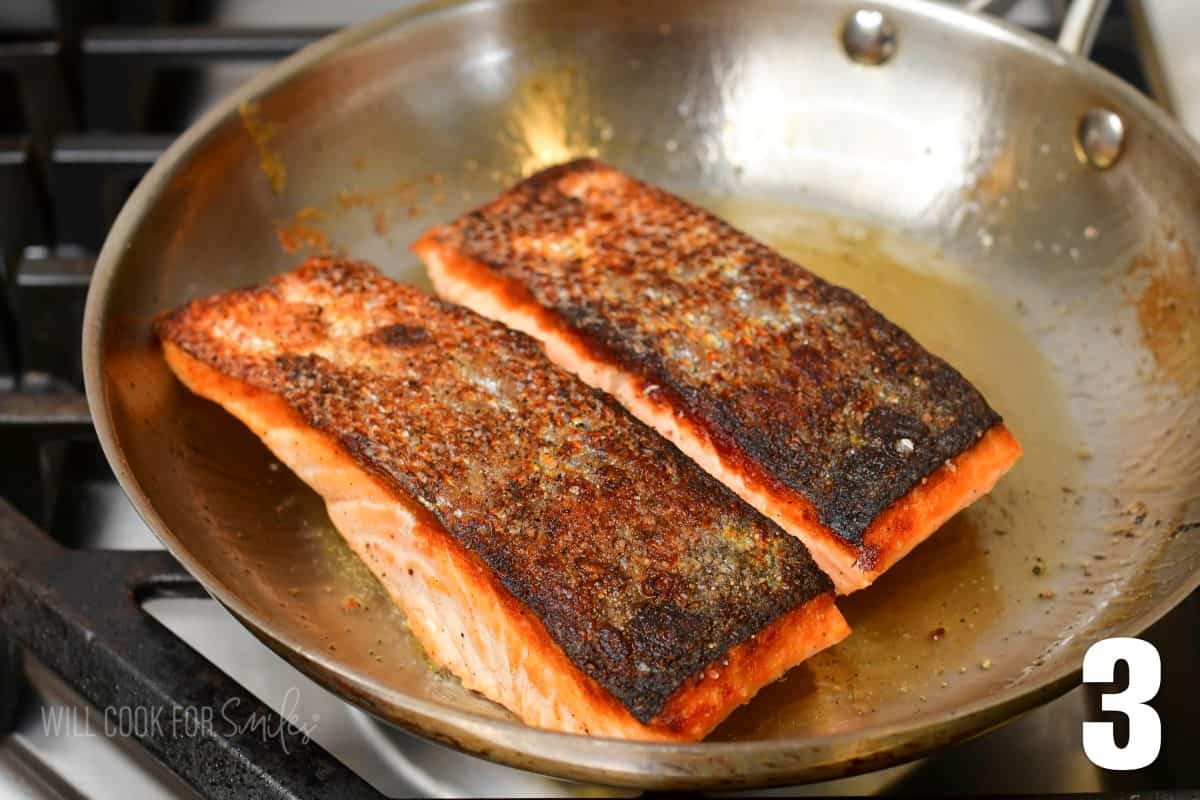 two crispy skin salmon filets in a stainless steel pan skin side up.