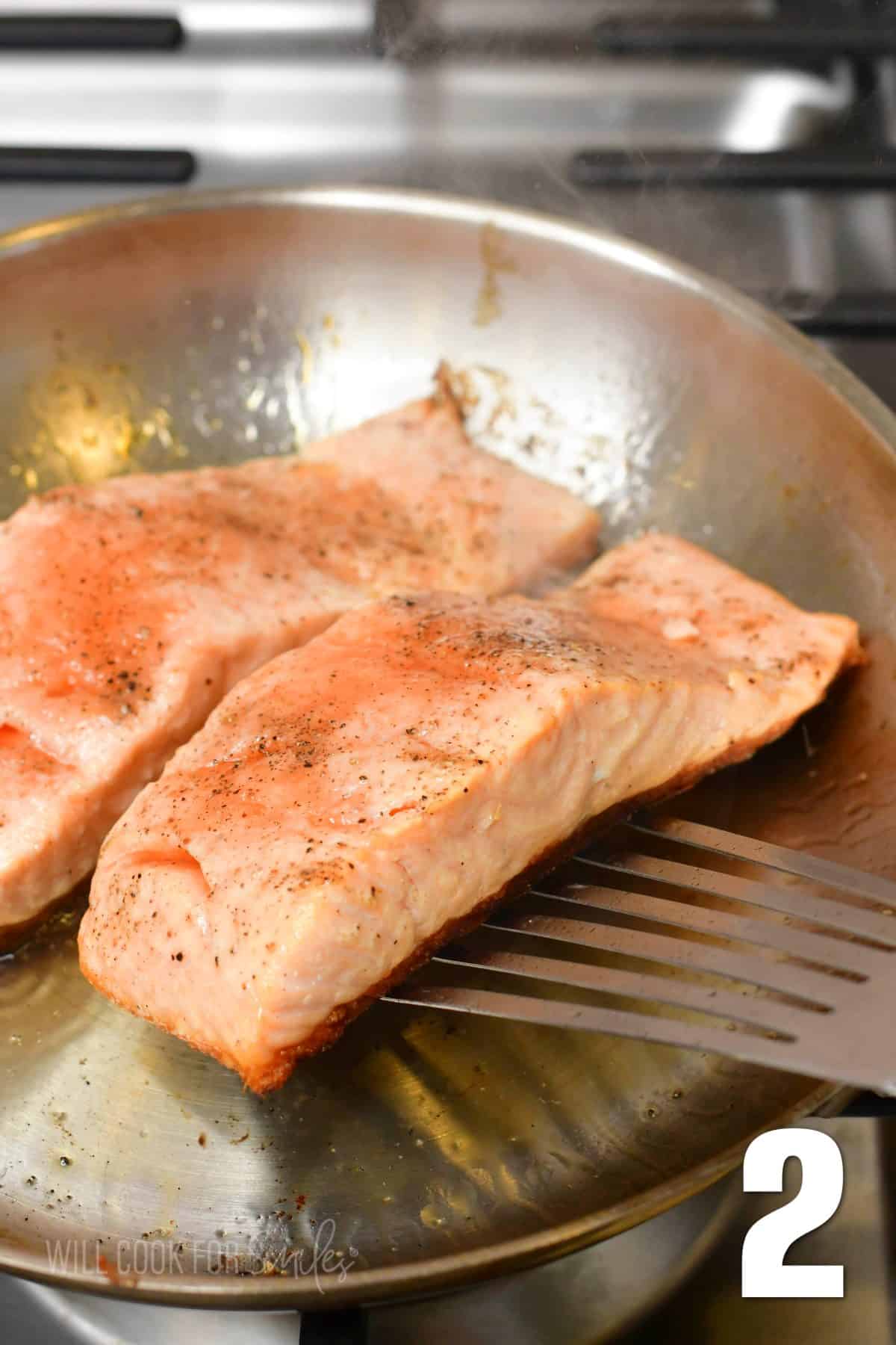 flipping a salmon filet in the pan with a fish spatula.