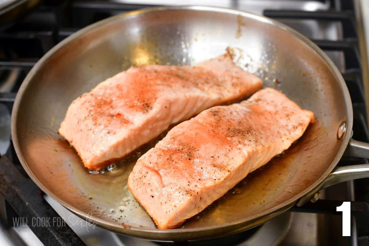 two salmon filets cooking in a steel pan skin side down.
