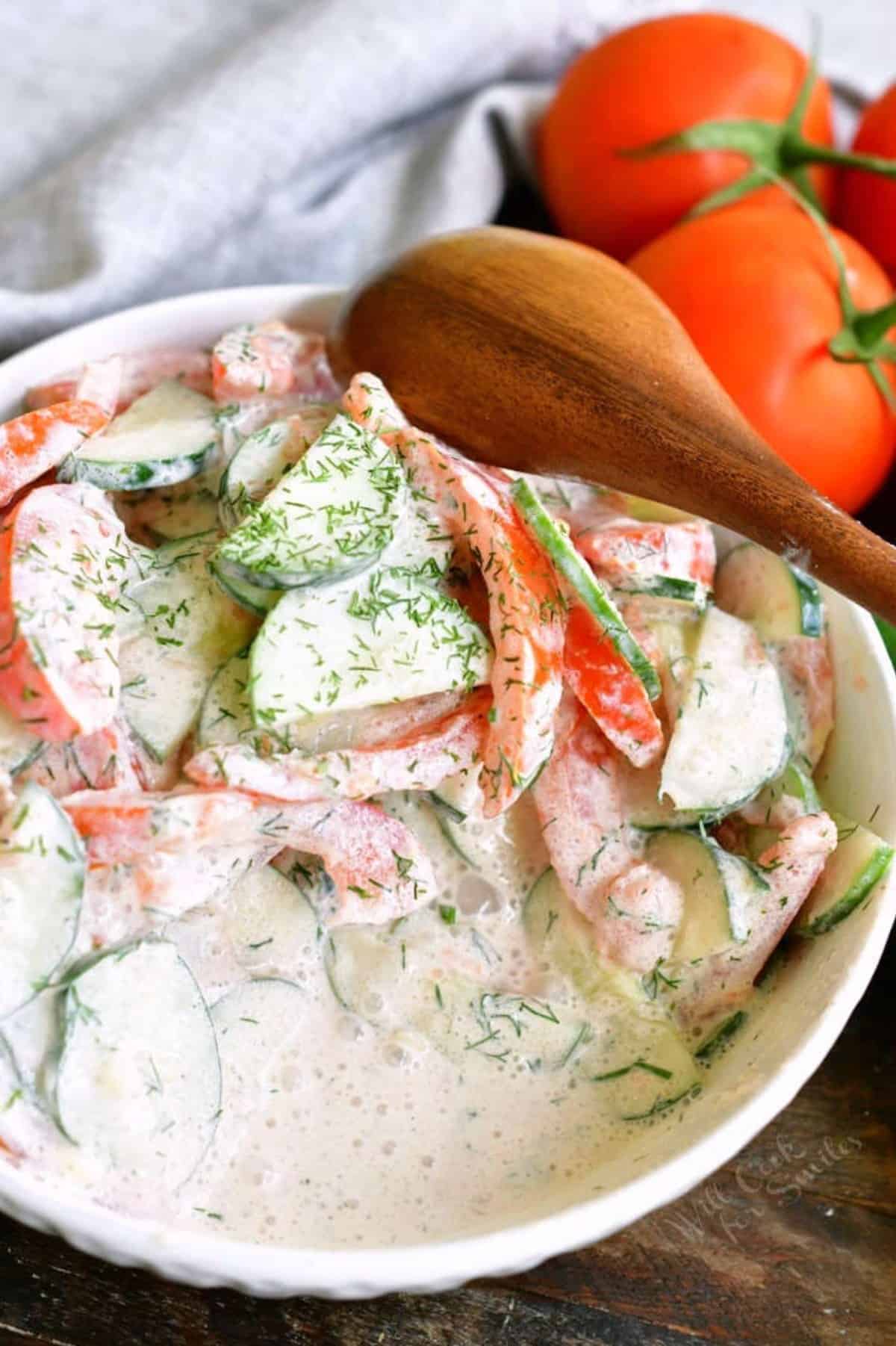 creamy tomato cucumber salad in a white bowl with some scooped out.