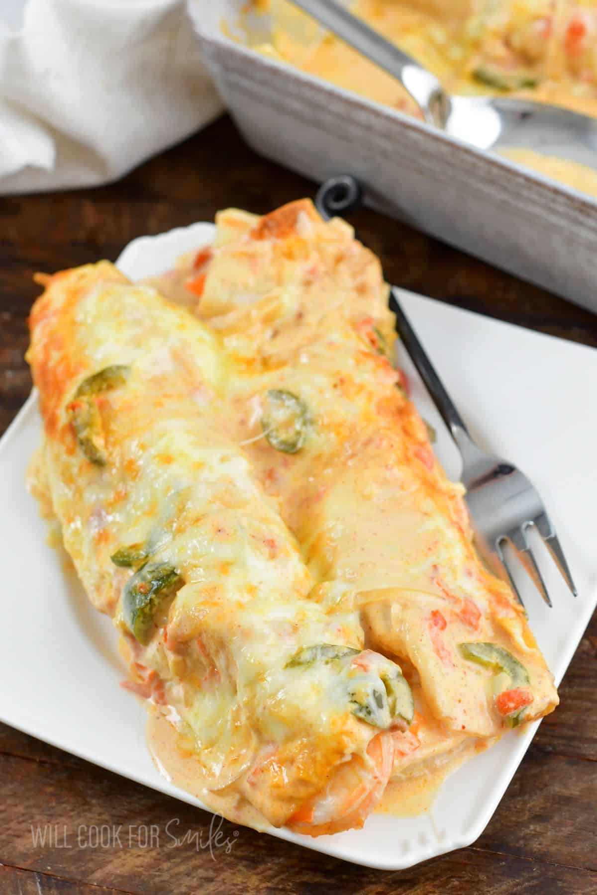 two shrimp enchiladas on a white plate with a fork.