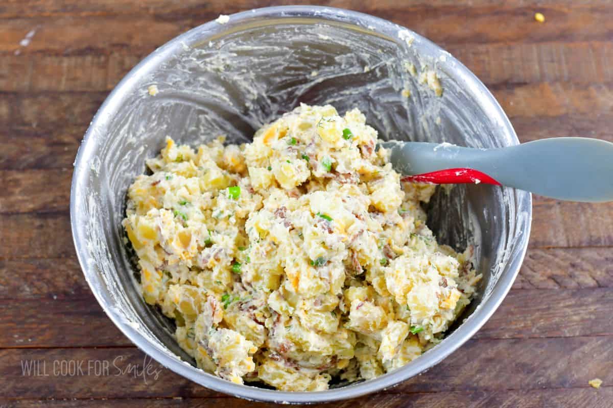 mixing loaded potato salad in a mixing bowl.