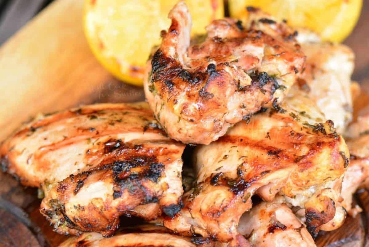 several stacked grilled marinated Greek chicken thighs on wooden plate.