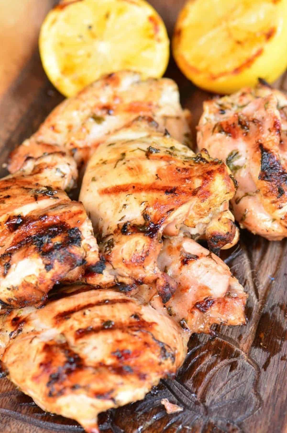 grilled marinated Greek chicken on wooden plate with lemon halves.
