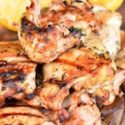grilled marinated Greek chicken thighs on wooden plate with lemon halves.