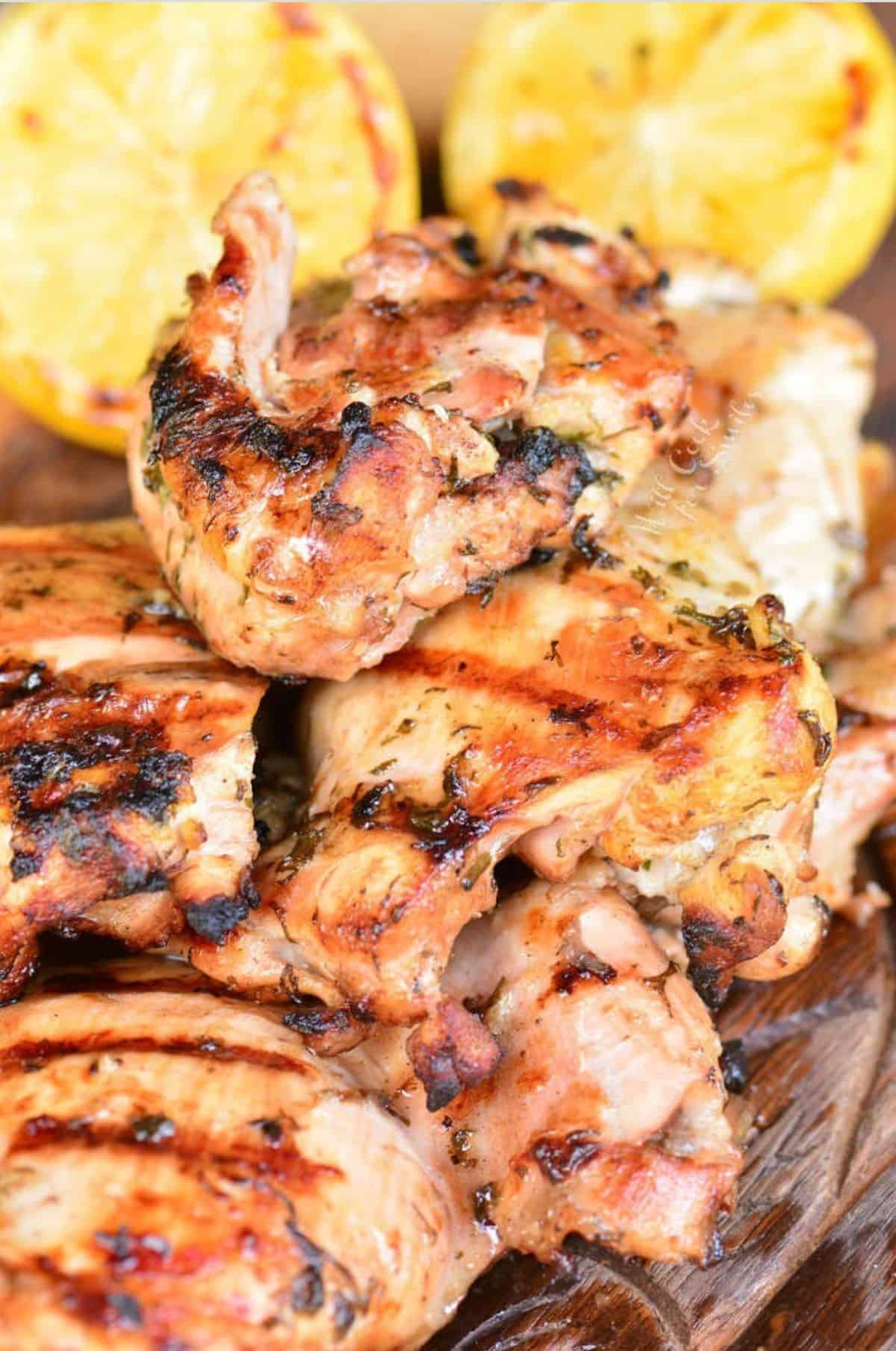 grilled marinated Greek chicken thighs on wooden plate with lemon halves.