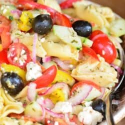 Greek tortellini salad in a brown bowl with a large spoon.