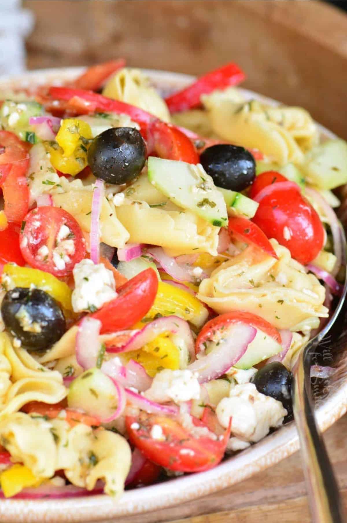 Greek tortellini salad in a brown bowl with a large spoon.