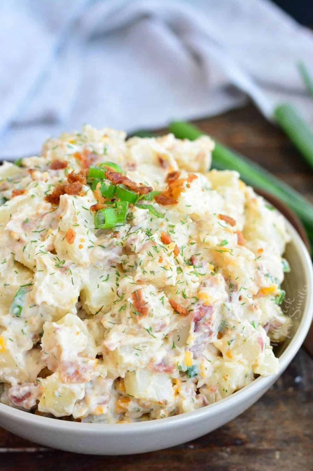 baked potato salad in a green bowl next to a towel and green onions.