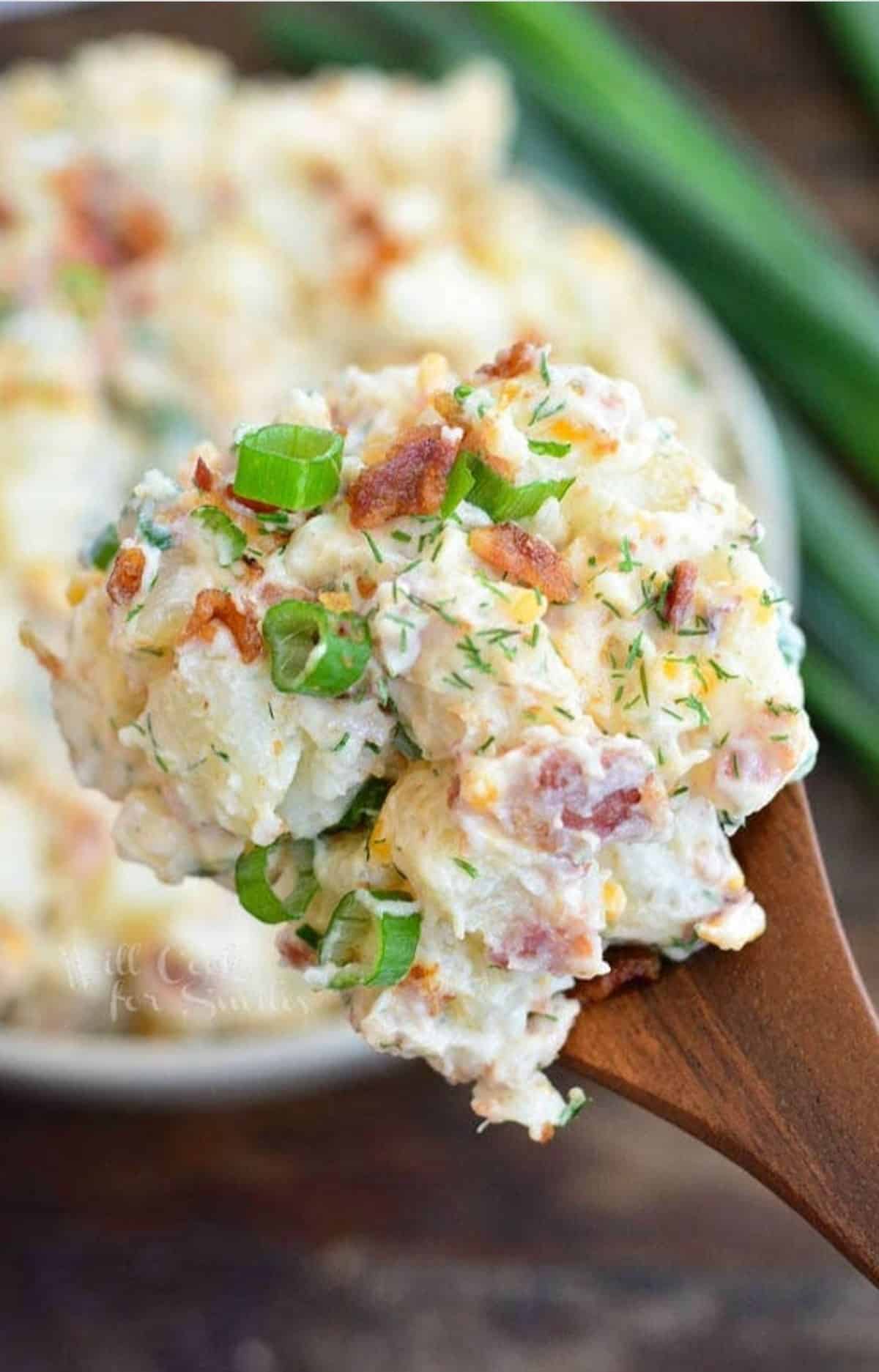 scooped loaded baked potato salad on top of a wooden spoon.