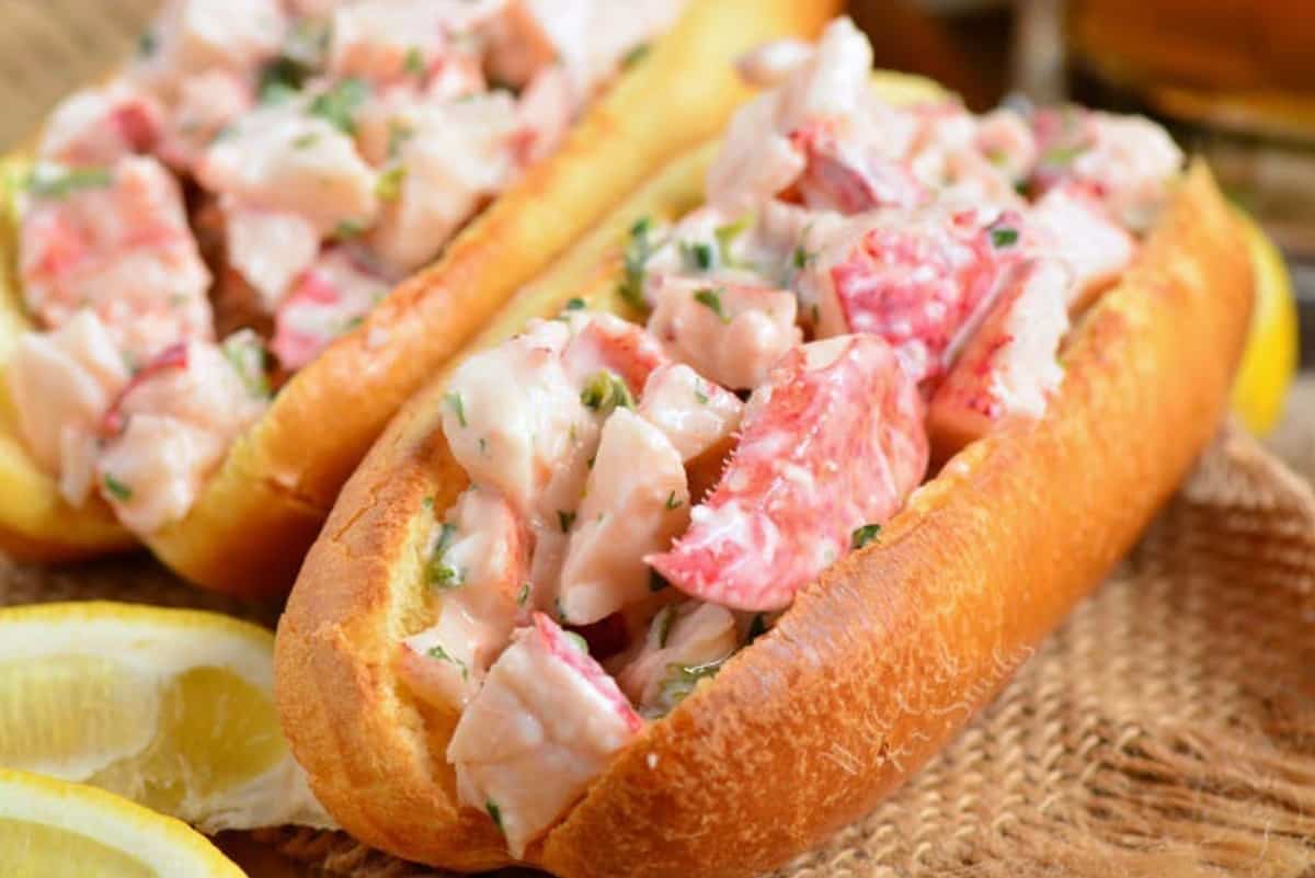 hot dog bun filled with lobster mixture and one on background.