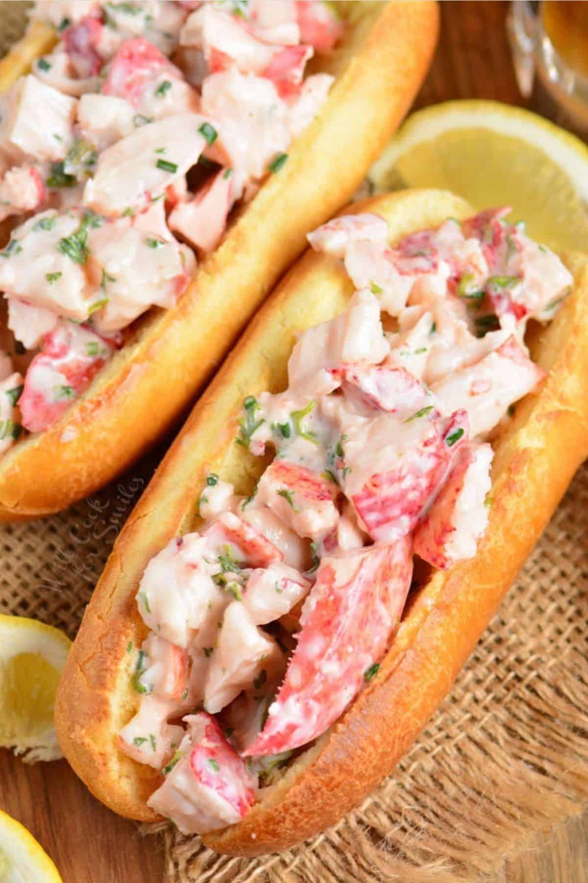 two hot dog buns filled with lobster mixture and lemon wedges.