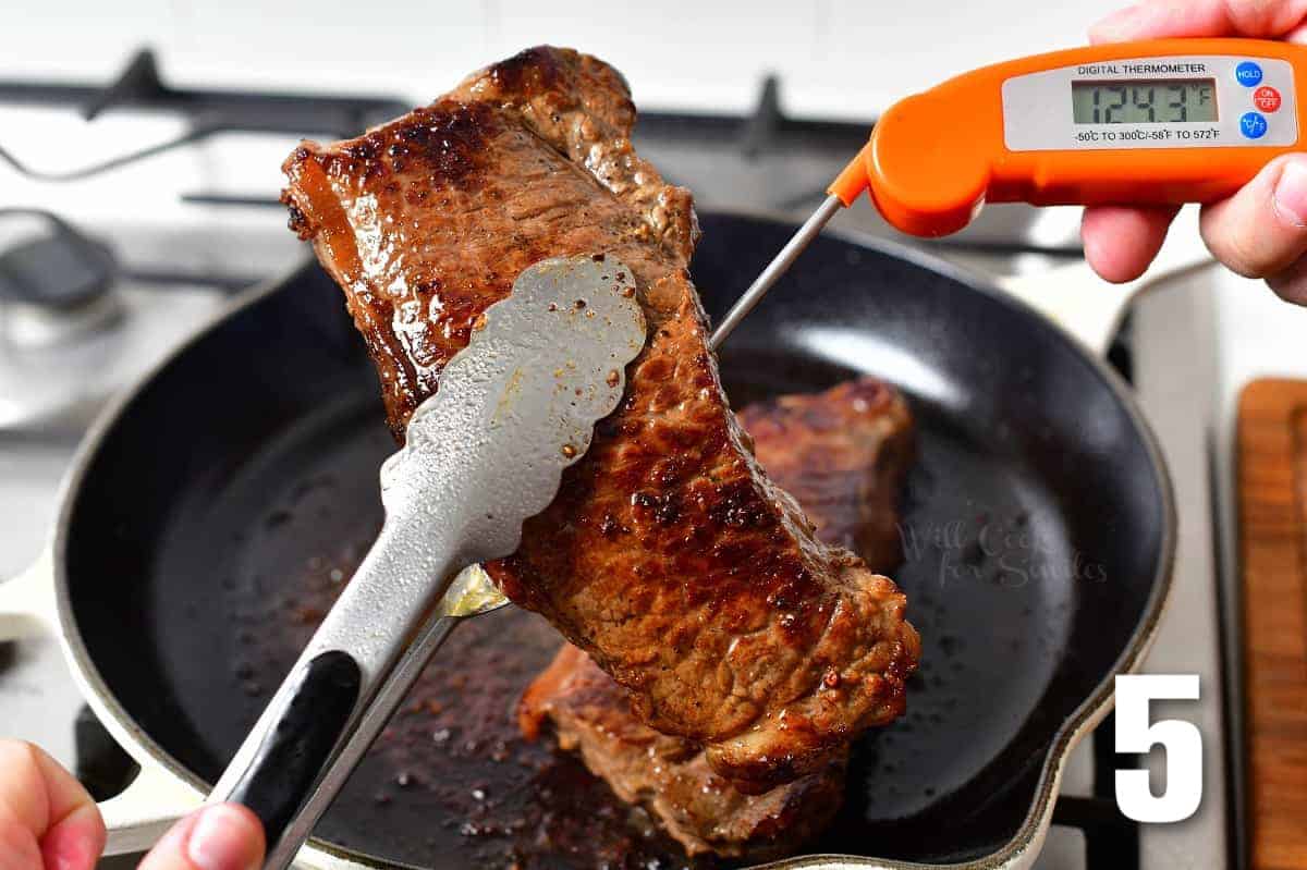 holding a teak with tongs and taking a temperature of it.