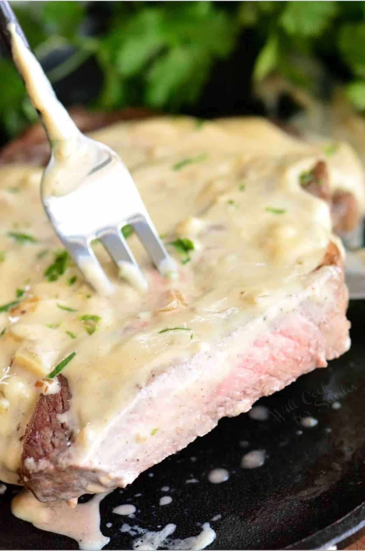 holding a sliced ribeye steak with cream sauce with a fork.