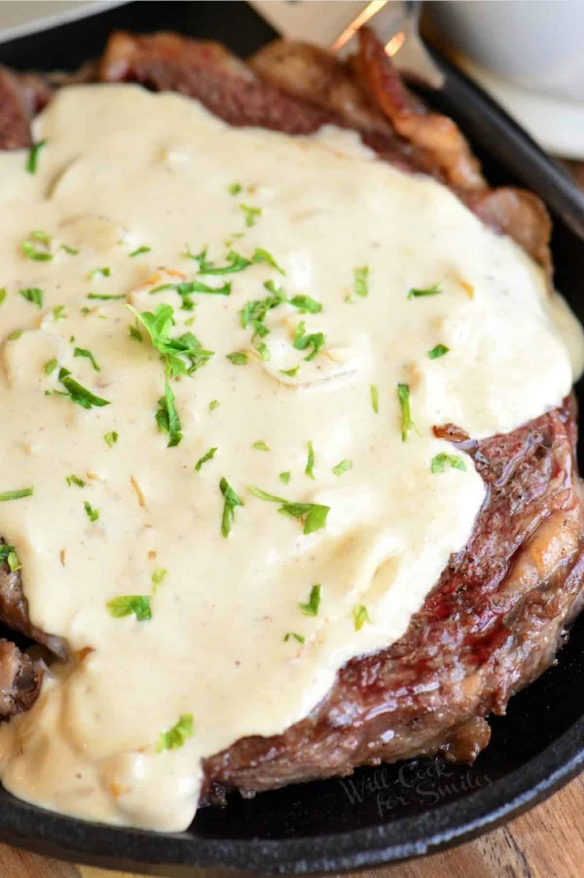 ribeye steak on a cast iron plate with creamy sauce over it.