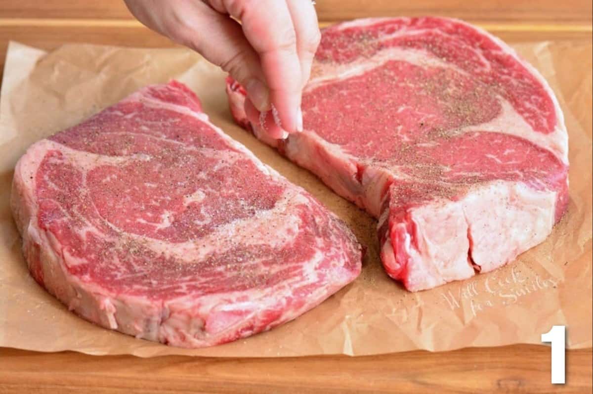 seasoning two ribeye steaks with salt and pepper on parchment paper.