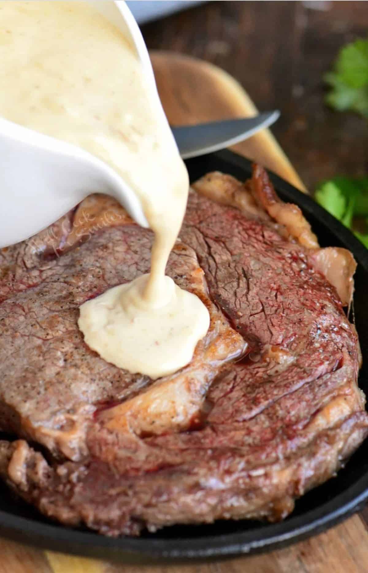 pouring creamy steak sauce over the seared ribeye steak.