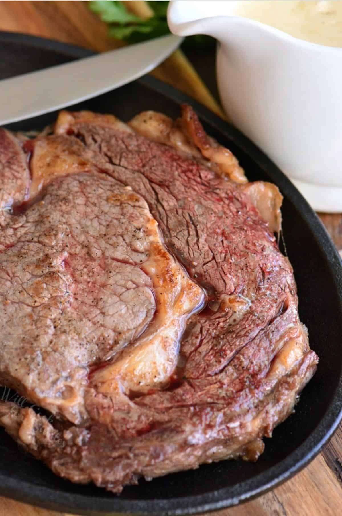 seared ribeye steak on a cast iron skillet with sauce next to it.