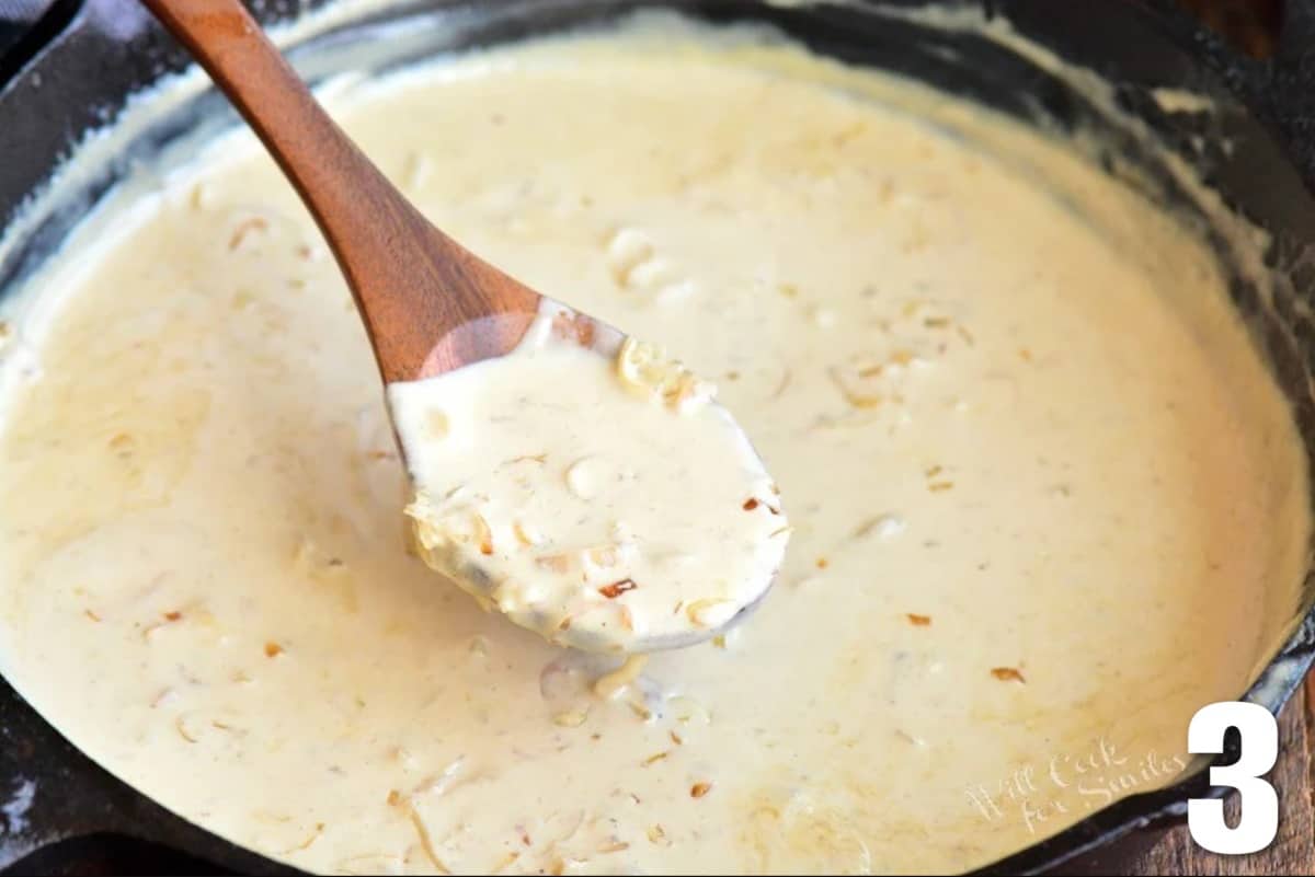 spooning out some creamy steak sauce from the pan with wooden spoon.