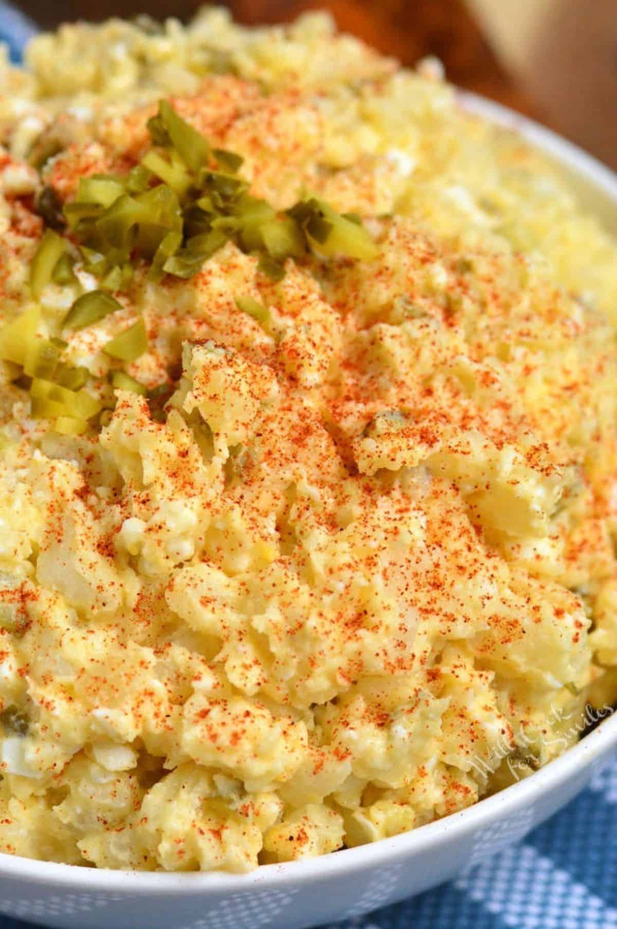 mixed southern potato salad in a white bowl with paprika and pickles.