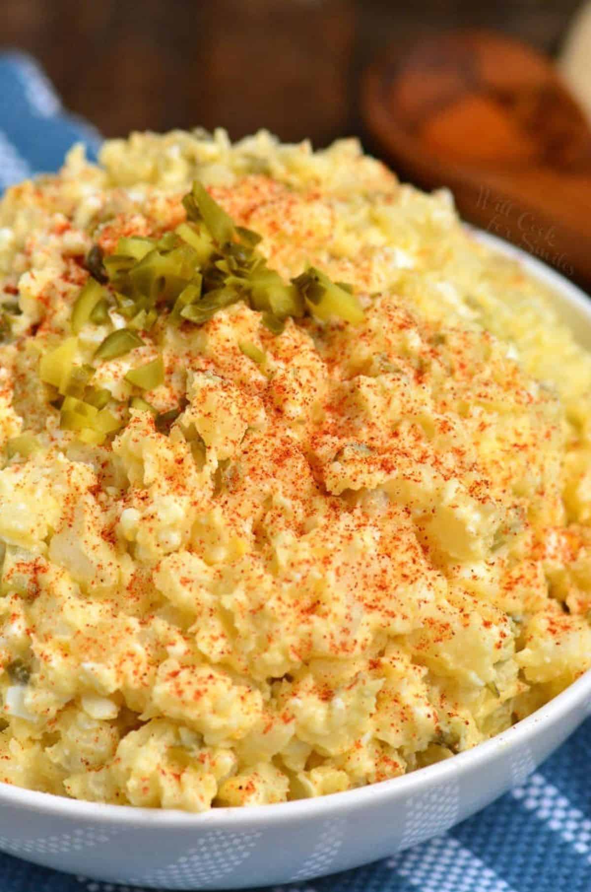 southern potato salad topped with paprika in a while bowl.