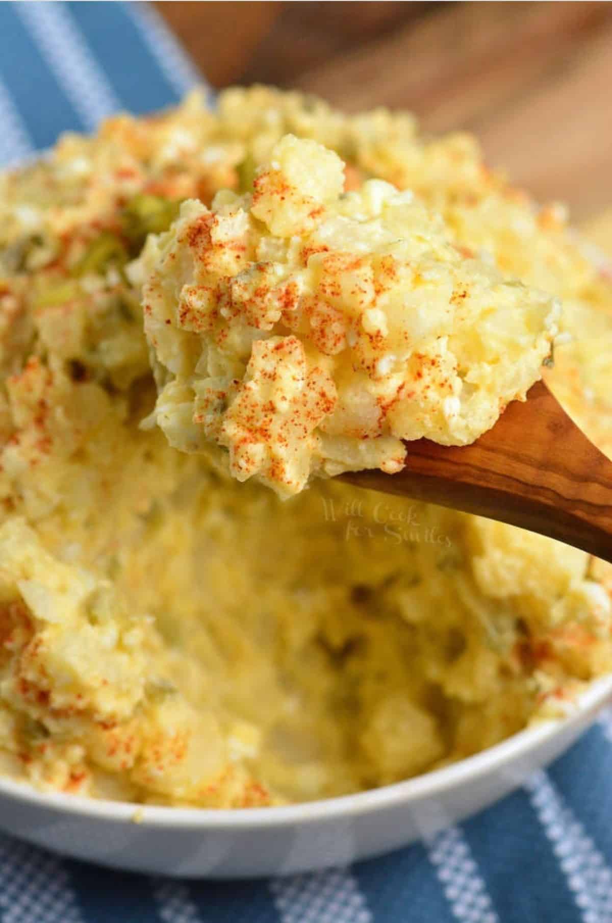 scooping southern potato salad with a wooden spoon out of the bowl.